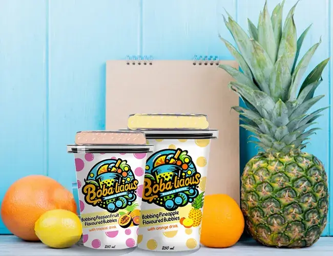 Bright and vibrant BobaLicious flavored bubble drinks on a wooden table, surrounded by fresh citrus fruits and pineapple, enhance the tropical theme.