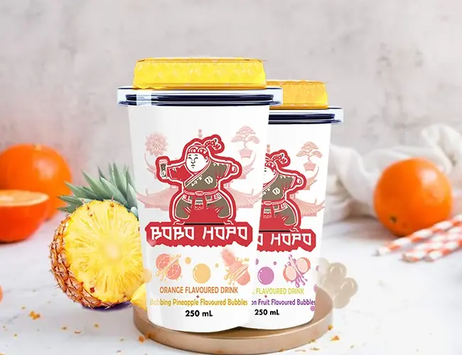 Bobo Hopo flavored bubble drinks in orange and tropical flavors are presented with fresh pineapples and oranges on a textured background.